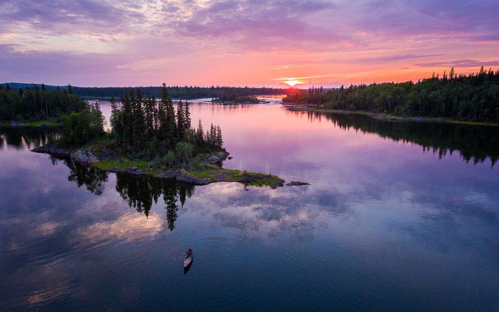 A peaceful sunset casts vibrant colors over a canoe gently drifting on a calm lake within the Churchill River system.