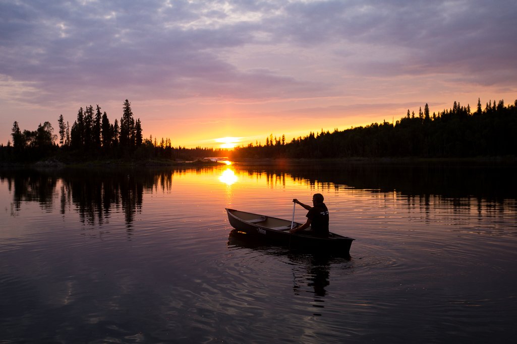 Person in a canoe paddling on a calm lake at sunset in northern Saskatchewan.