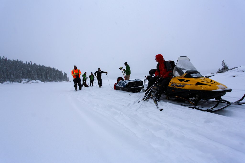 a group of people with cross-country skis and a couple snowmobiles out on the snow in northern saskatchewan in winter