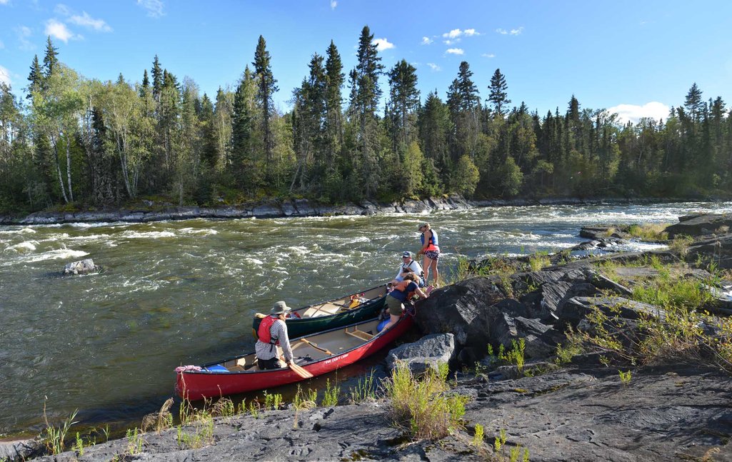 A few people and a couple canoes on a rocky shore next to the Churchill River