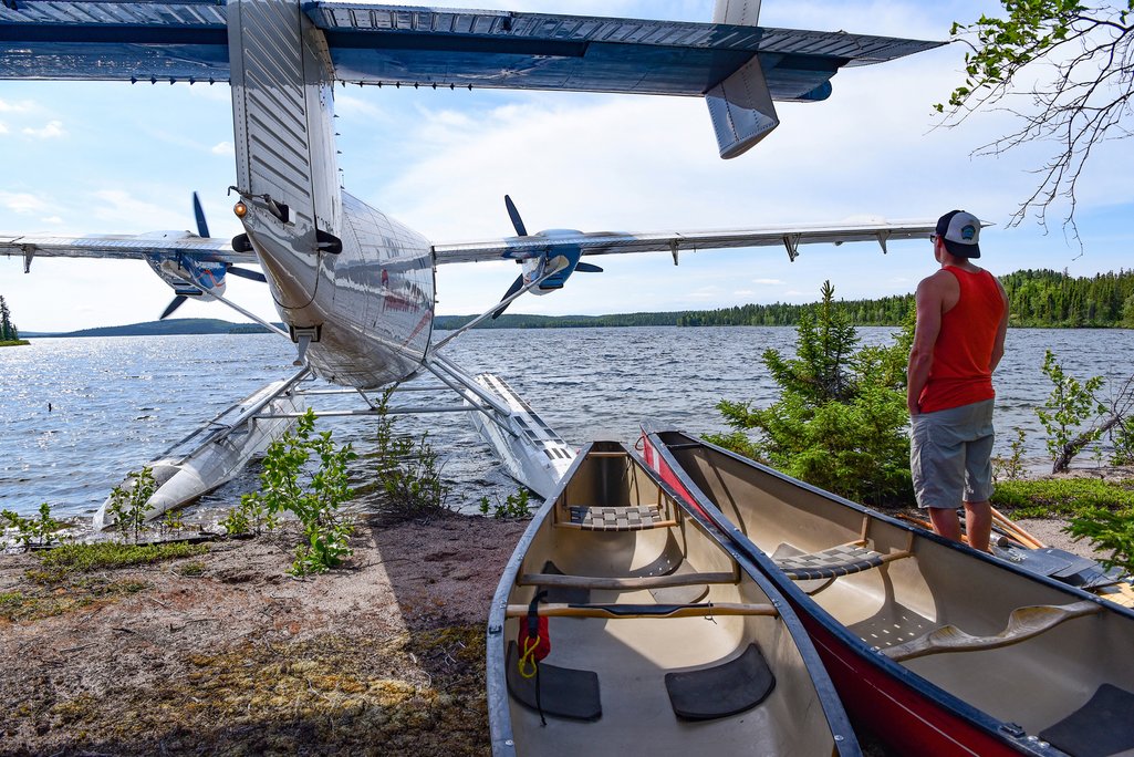 person standing by floatplane parked on shore of remote northern saskatchewan lake