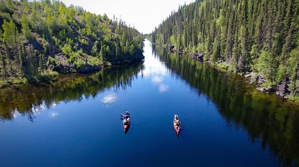 aerial view of two canoes paddling down a calm river surrounded by Canadian shield forest