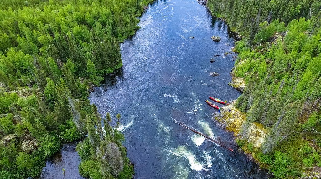 aerial top down view of a river with forest on both sides and two canoes on a rocky shore