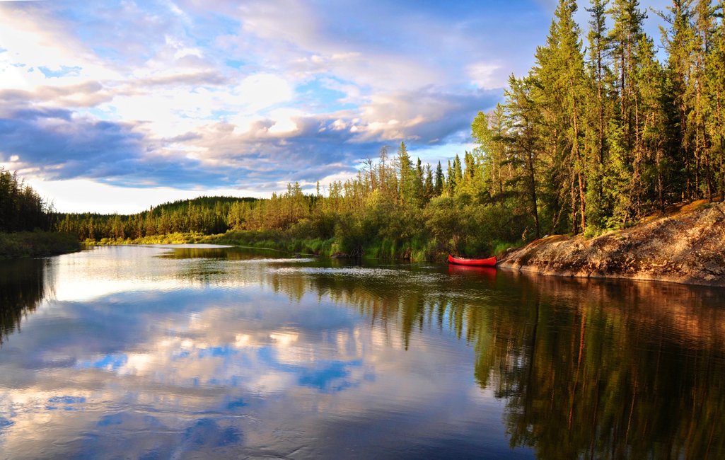 golden hour photo of a calm river with a canoe on the other side n northern saskatchewan