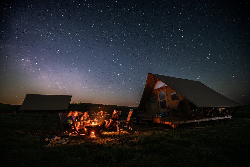 A group of people sitting around a campfire beside a Parks Canada oTENTik under a starry night sky