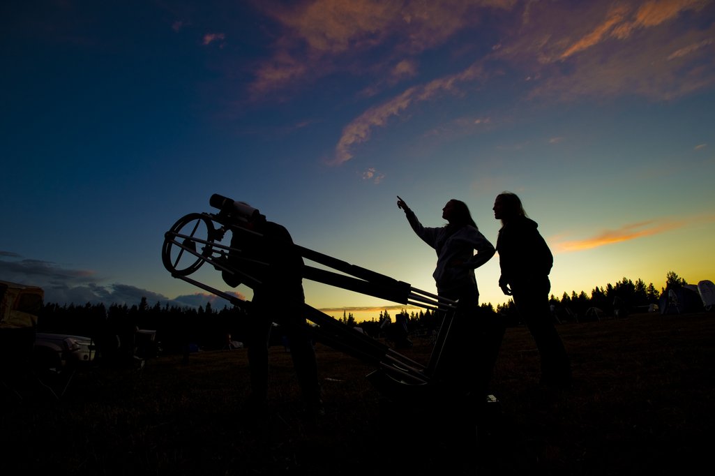 Astronomers beside a telescope pointing at the almost dark sky with some stars appearing