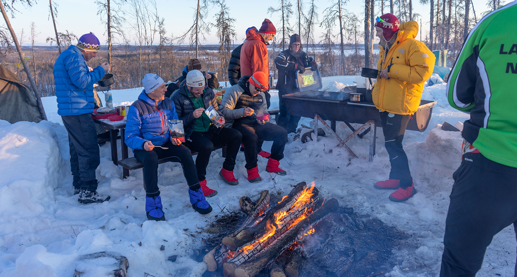 A group of tired skiers are gathered around a campfire as the sun goes down at the Don Allen Saskaloppet in La Ronge, Saskatchewan