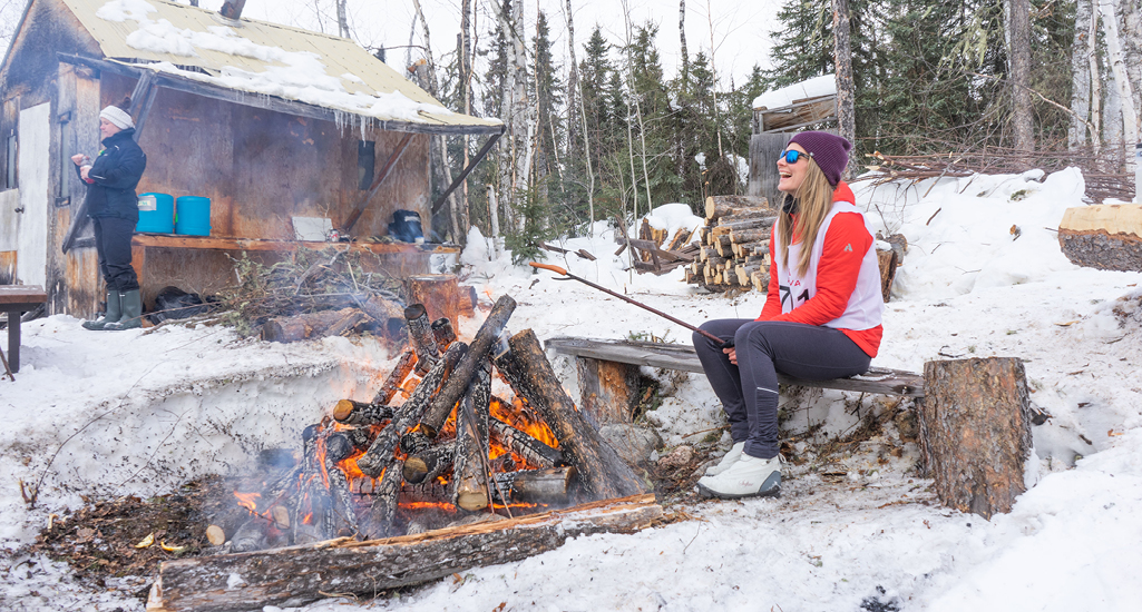 Ashlyn George is roasting a hot dog over an open fire at one of the rest stops during the Don Allen Saskaloppet in La Ronge Saskatchewan