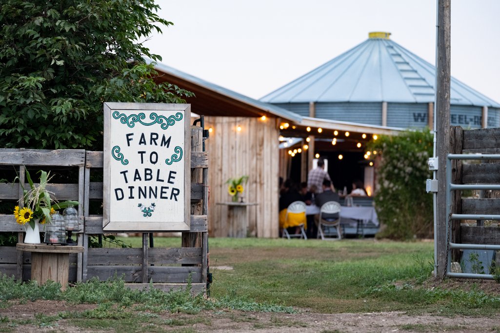 picture of Farm One Forty with a sign that reads, Farm to Table Dinner and a outdoor/indoor dining area with string lights