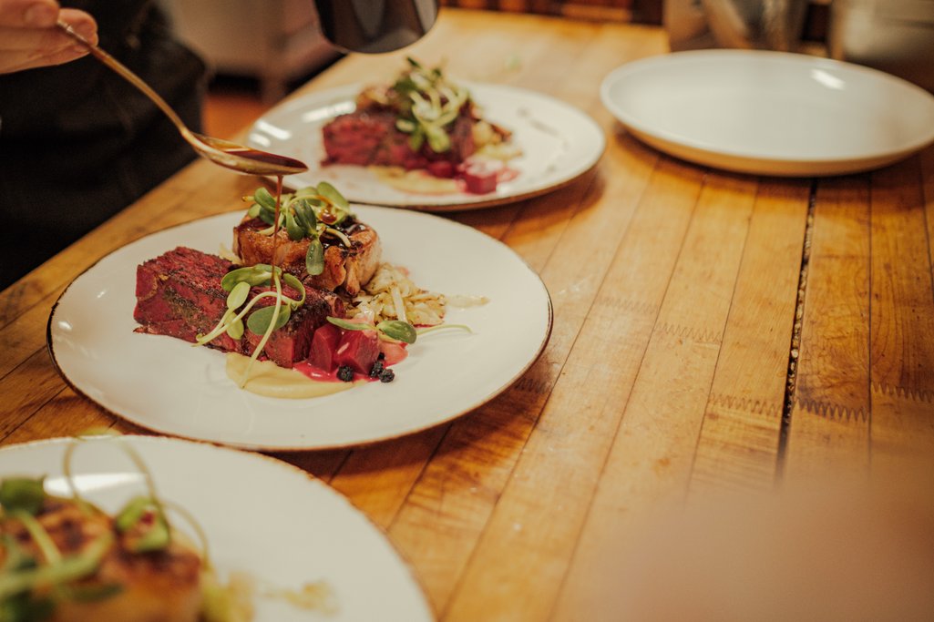 Picture of plates of food with a chef pouring a sauce on top