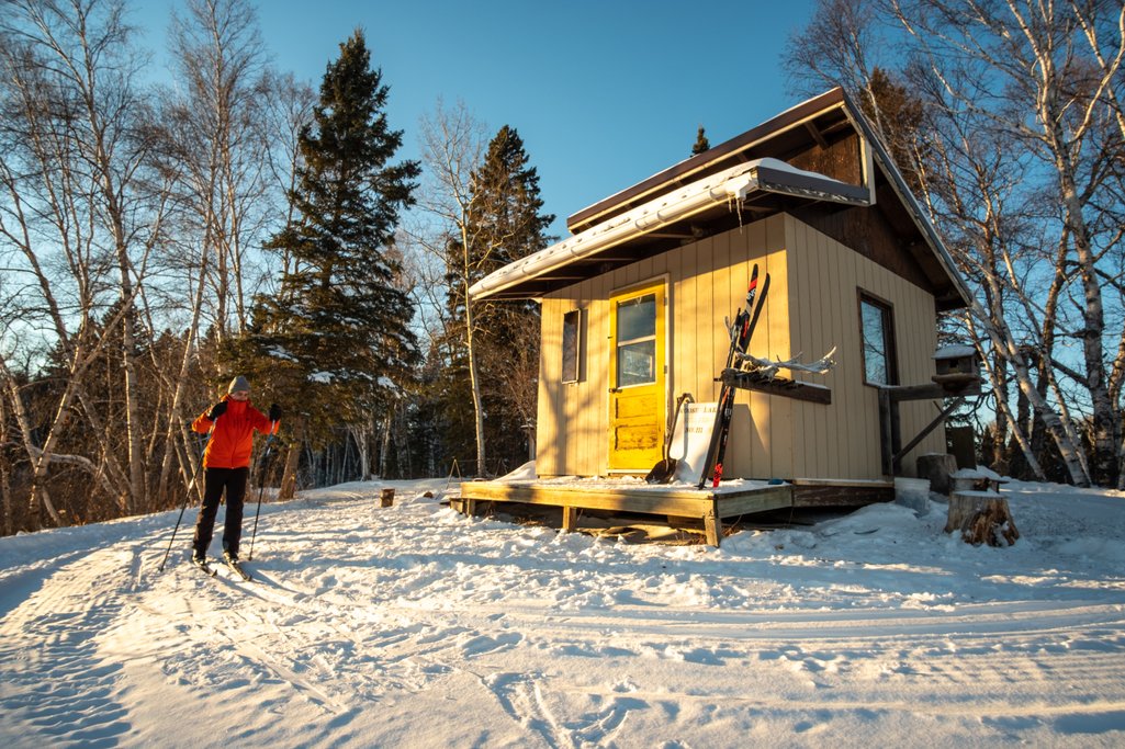 person in red jacket cross-country skiing on a track going around a warmup shelter