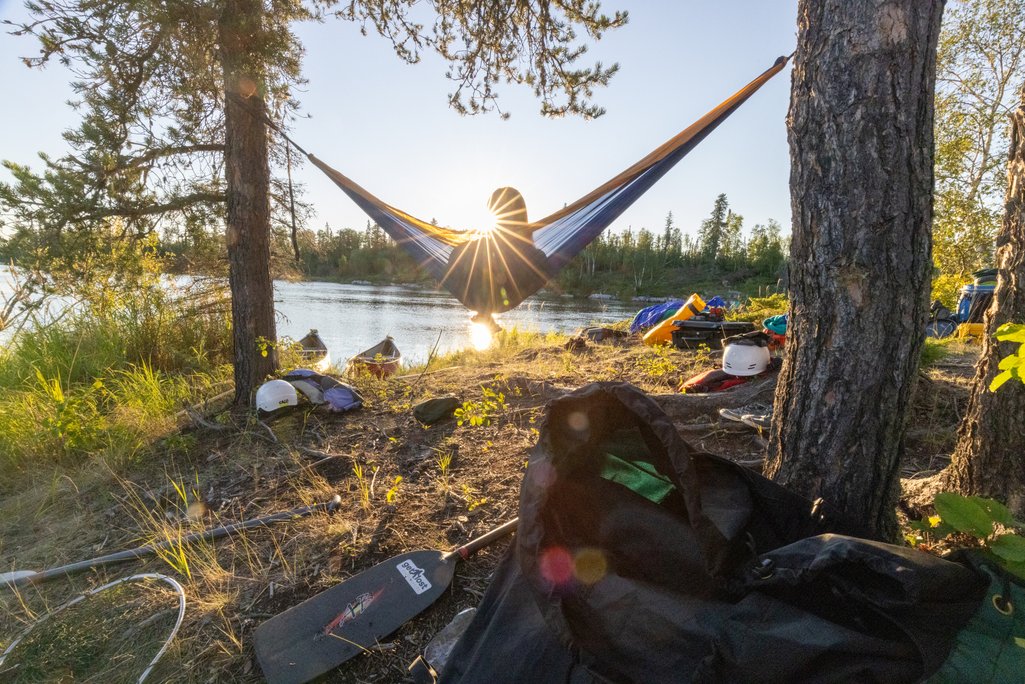 picture of a person relaxing in a hammock tied to two trees beside the churchill river in remote northern saskatchewan