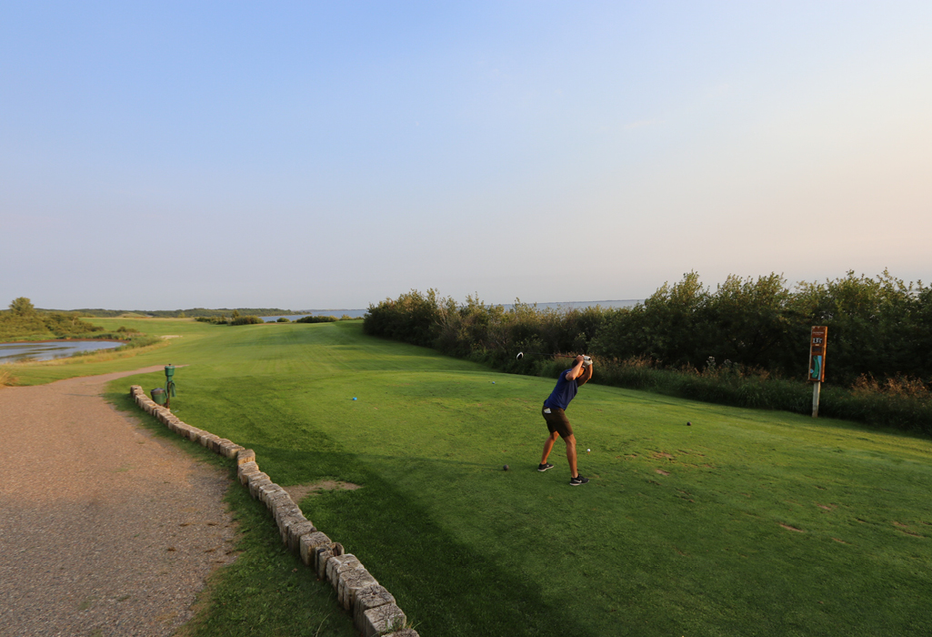 Person mid swing teeing off at Jackfish golf course