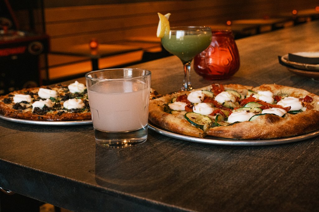 picture of two pizzas and a couple cocktails on a table