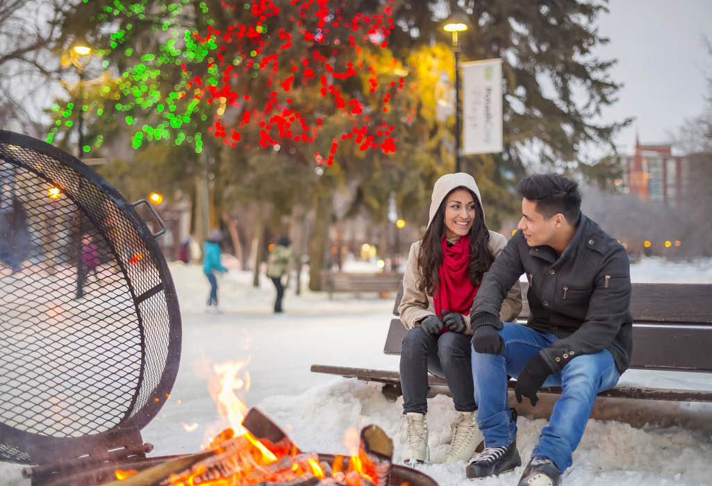 couple warming up by a fire outside at saskatoon outdoor rink