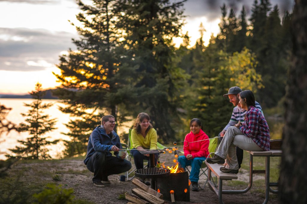 group of people gathered around a campfire with a lake in the background and surrounded by forest