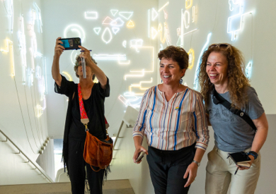 Three happy women in a modern art museum staircase with neon light art on the walls